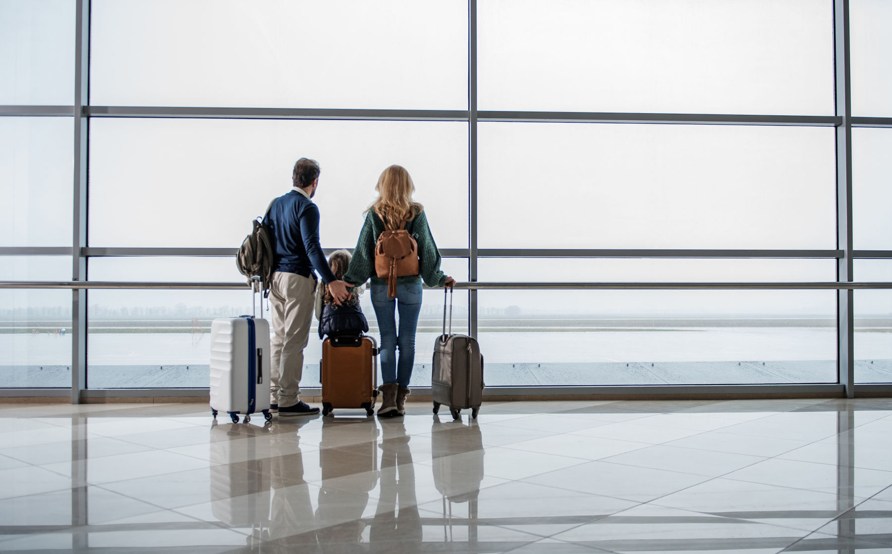 Famille avec ses valises devant une baie vitrée d'aéroport